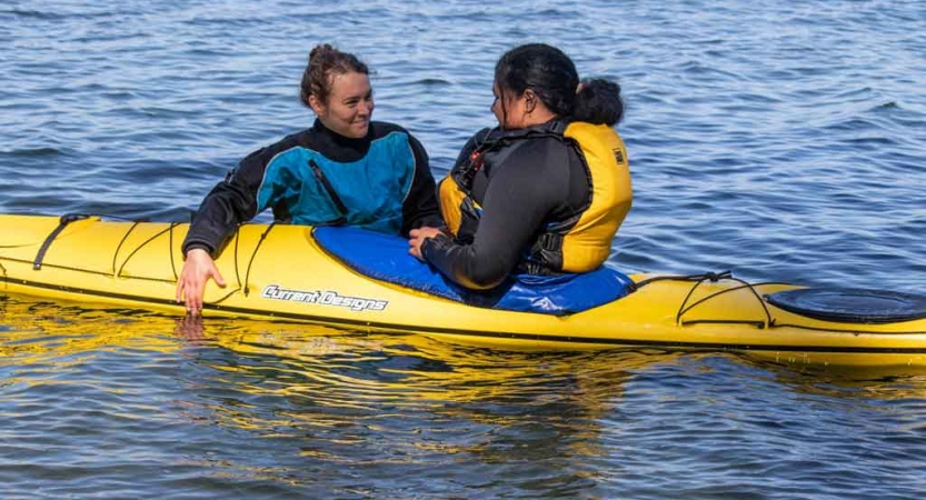 an instructor gives direction to a student in a kayak on an outward bound trip